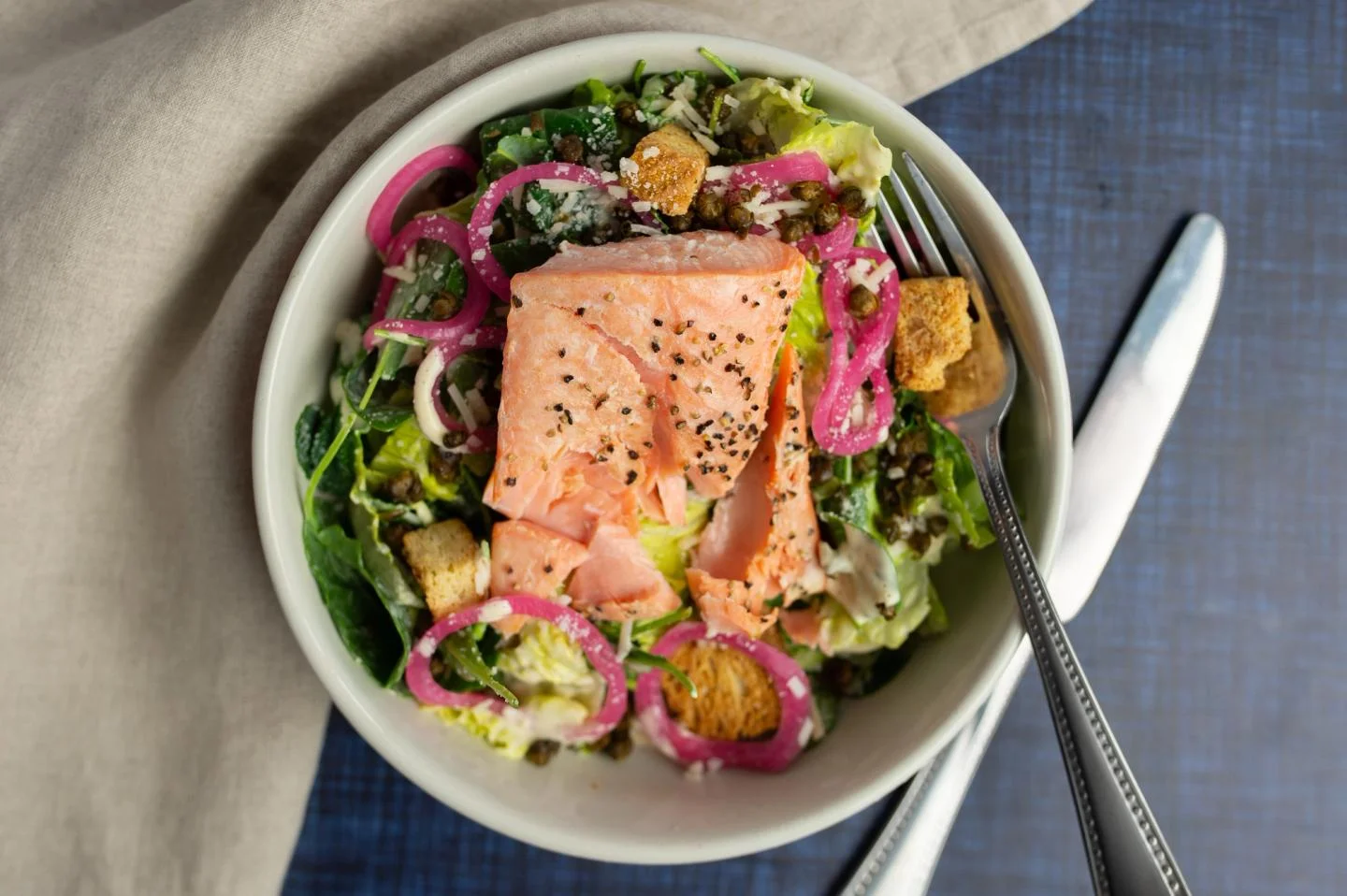 Bowl of salad with salmon, greens, croutons, and pickled onions.